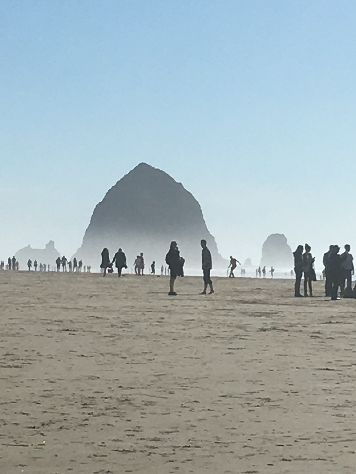 People in a sandy area by large mountains